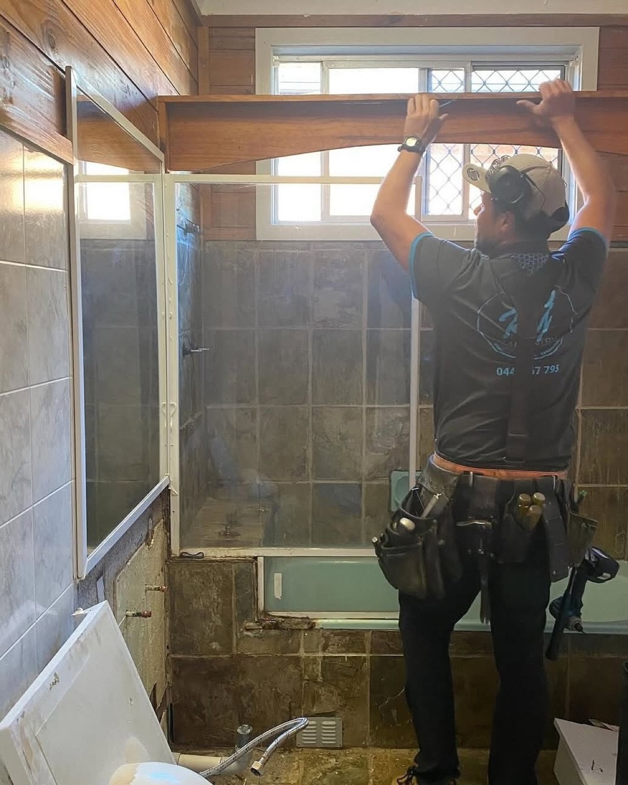 A carpenter fitting a glass shower screen into a part-finished bathroom
