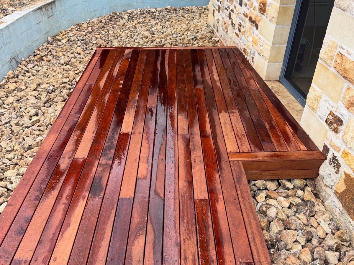 A hardwood deck laid against a stone wall with a pebble surround