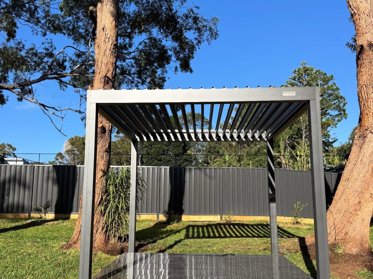 A freestanding pergola with a louvred roof standing on a lawn between gum trees