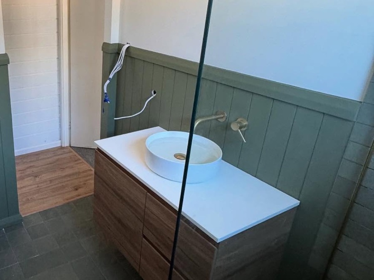 A finished bathroom with a timber vanity, glass screen and panelled walls
