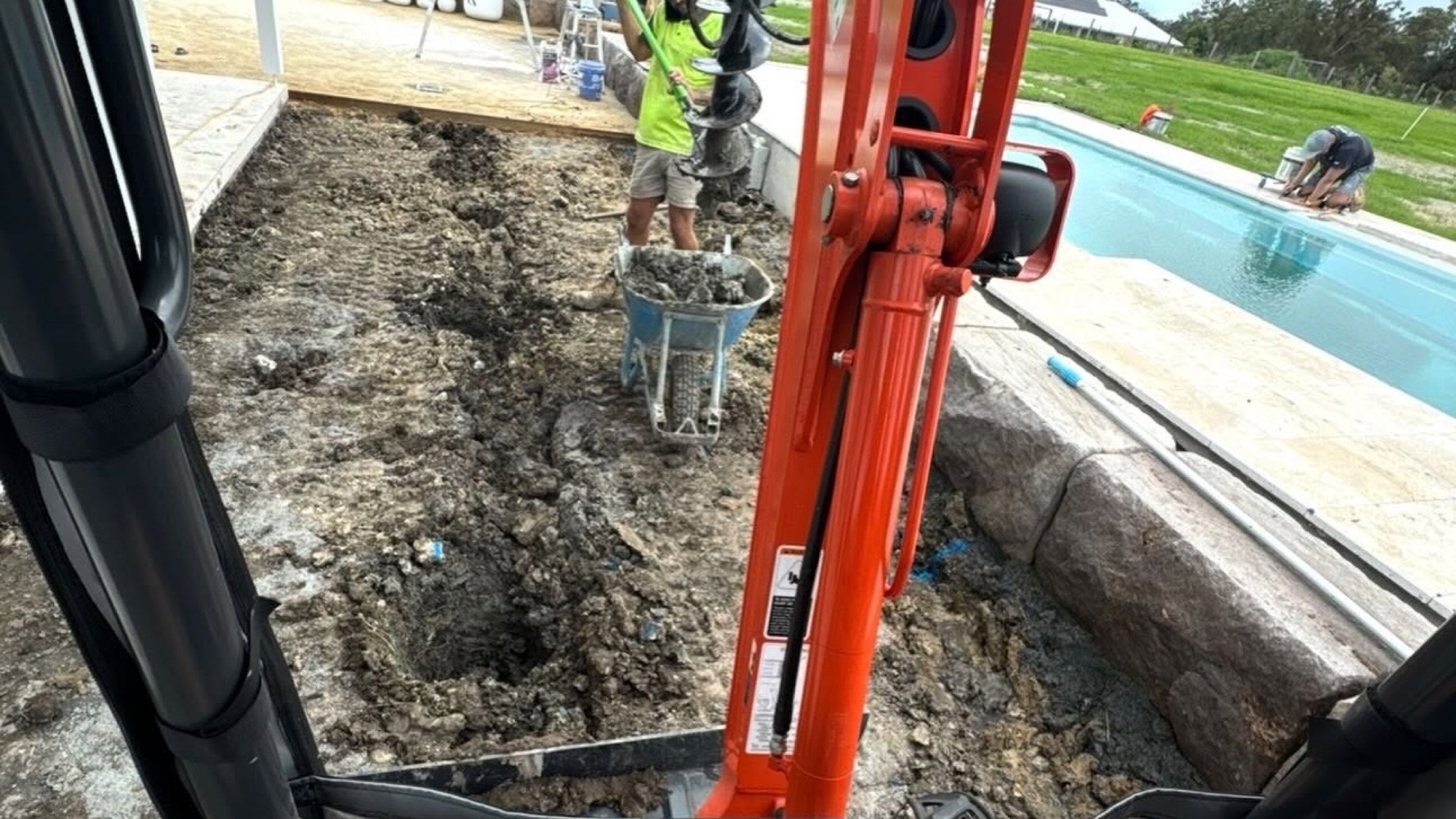 An excavator cutting into a sloped site beside a swimming pool