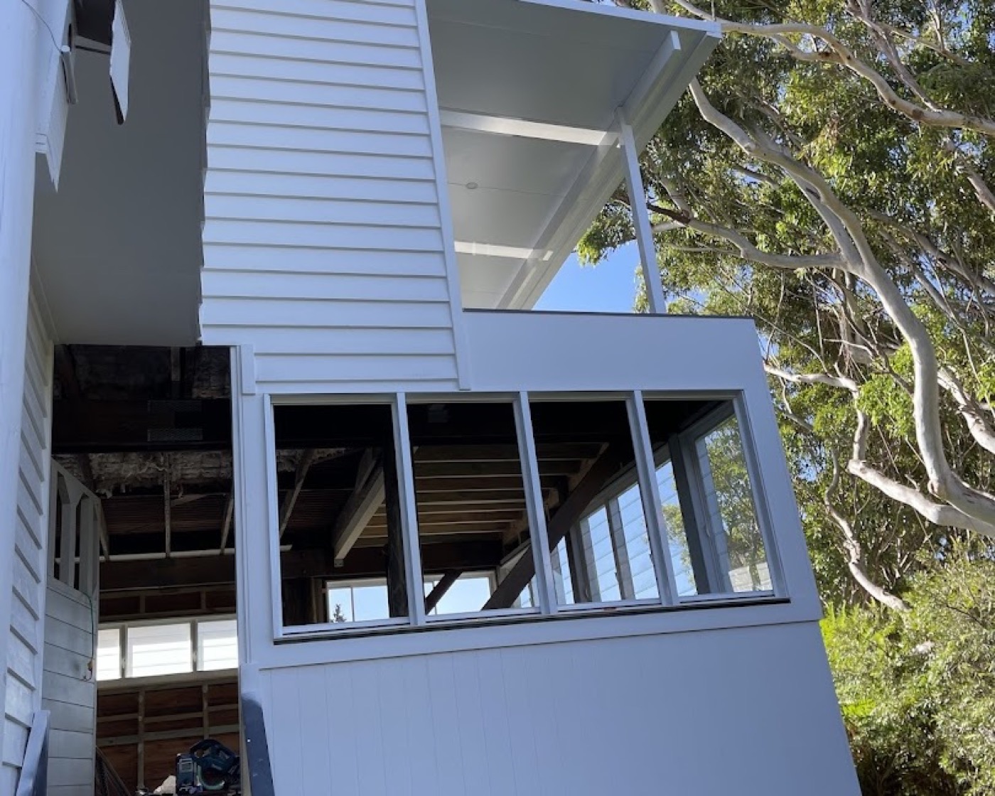 A weatherboard wall with new window openings framed up under a tree canopy