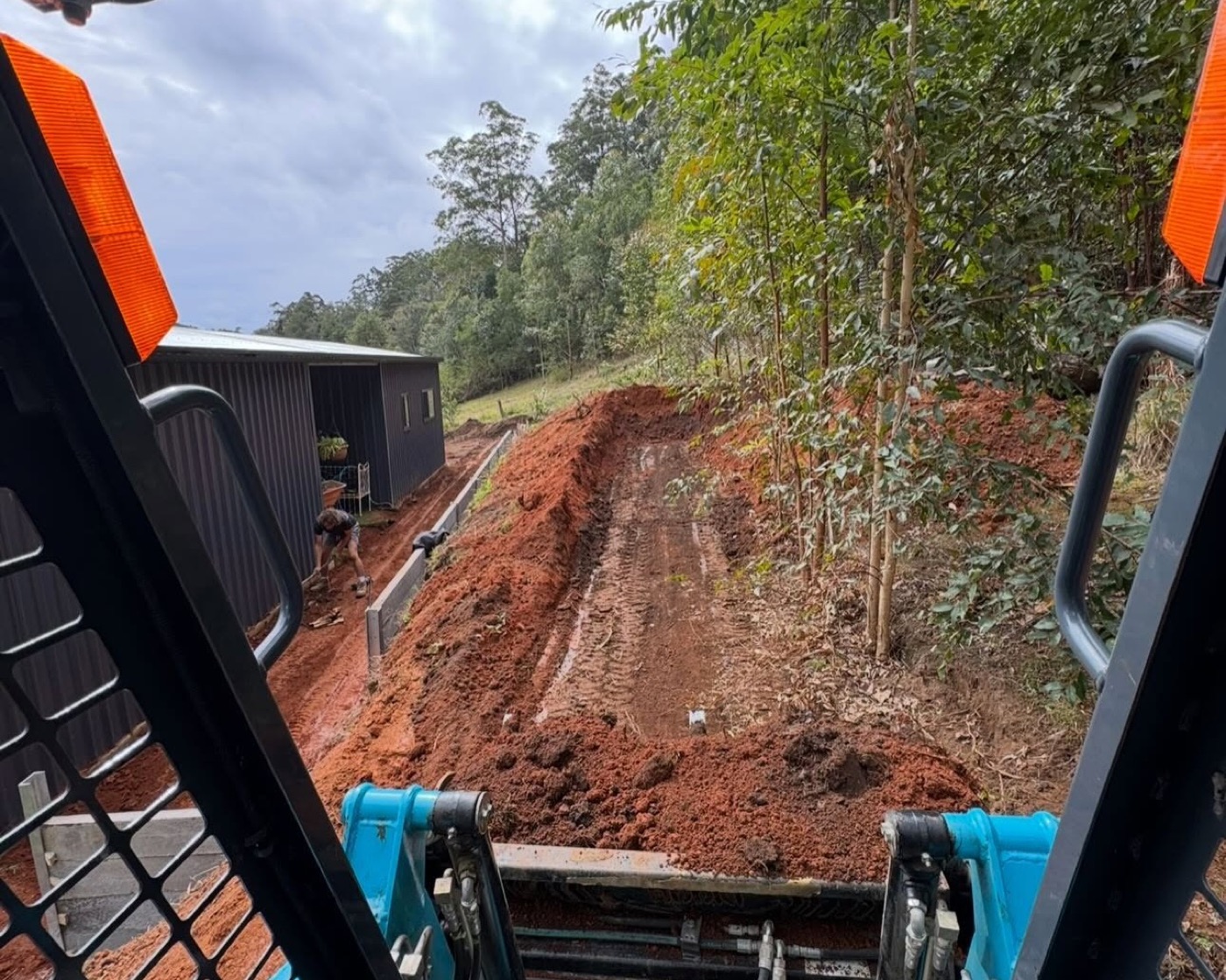 An excavator cutting a level bench into a steep red earth slope