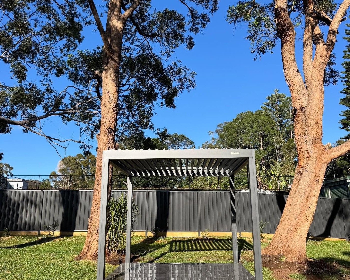 A pergola frame standing on a lawn beneath tall gum trees