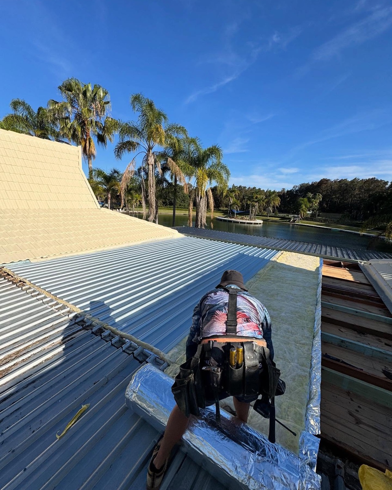 A carpenter kneeling on a roof fixing sheeting into place