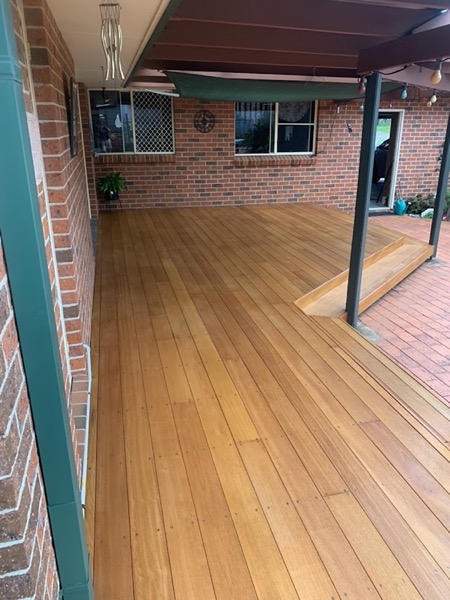A timber deck laid under a patio roof against a brick wall