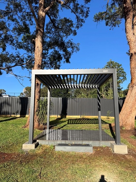 A freestanding pergola with a louvred roof standing on a lawn