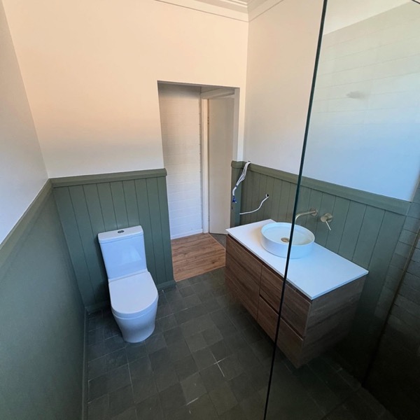 A bathroom with a timber vanity and a glass shower screen