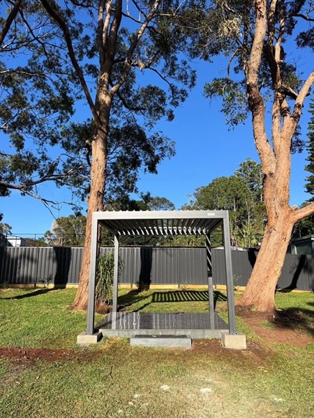 A pergola frame standing on a lawn under tall gum trees