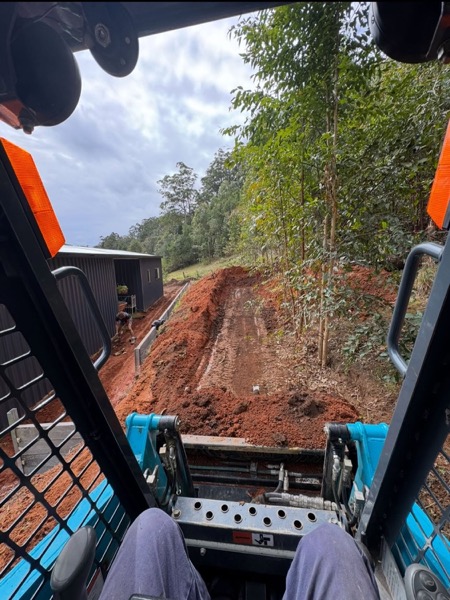An excavator cutting into a steep red earth slope
