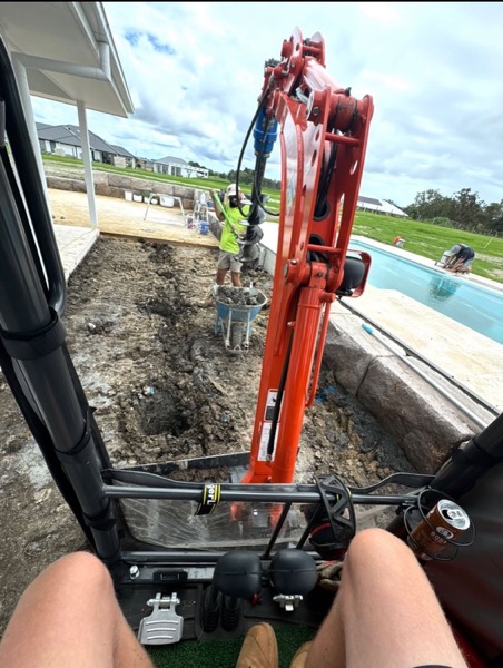 An excavator working on a cut beside a swimming pool