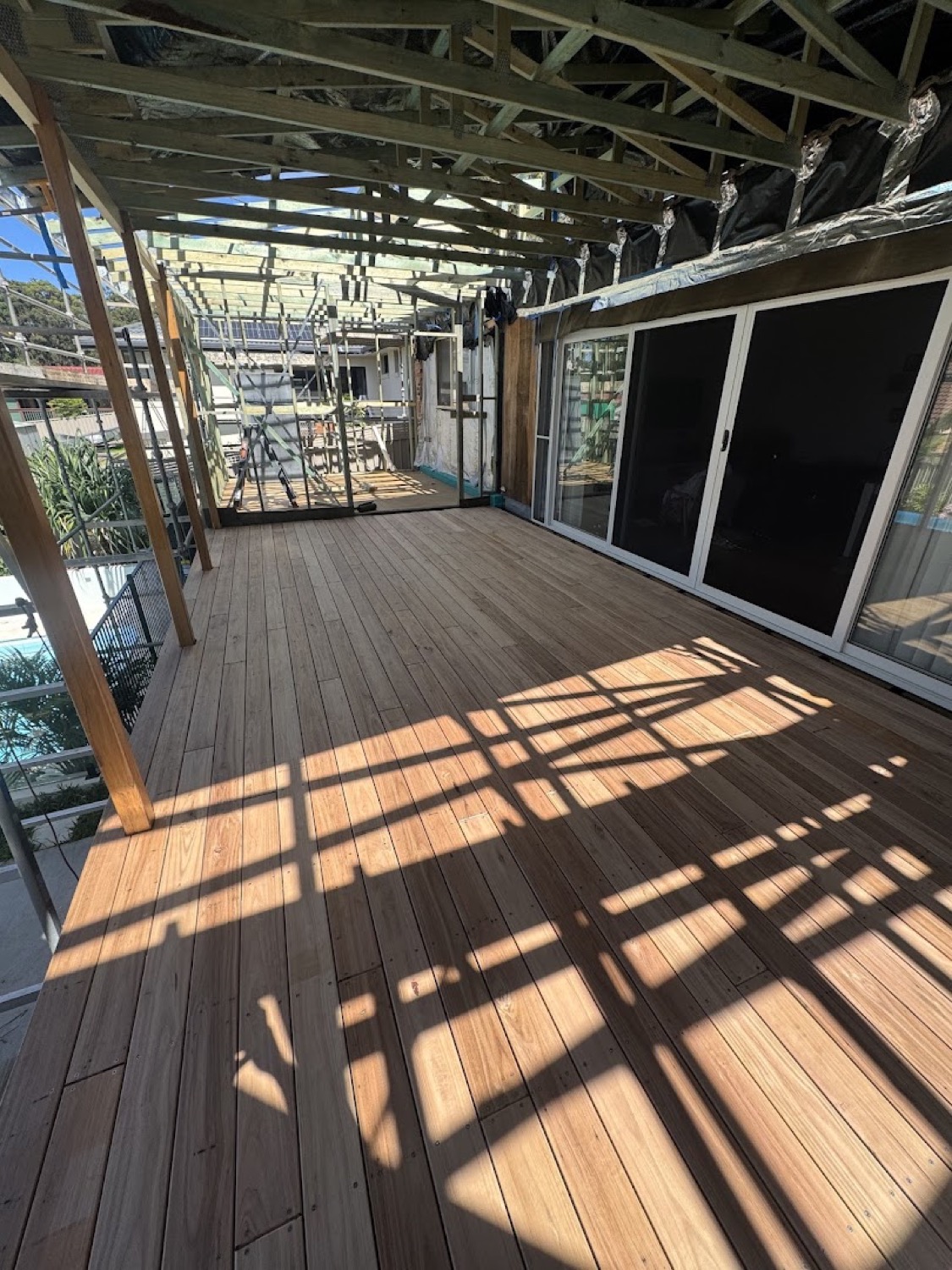 A hardwood deck under a slatted pergola with shadow lines across the boards